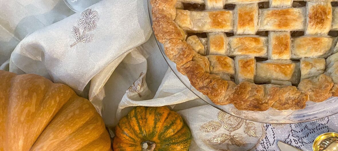 Image of apple pie and pumpkins on a white tablecloth.