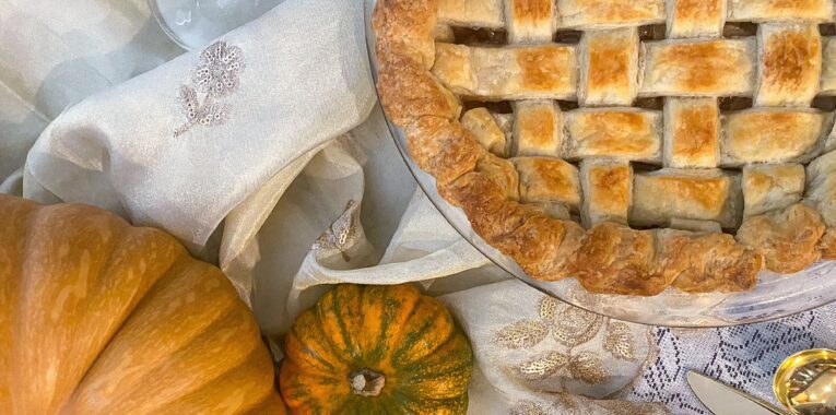 Image of apple pie and pumpkins on a white tablecloth.