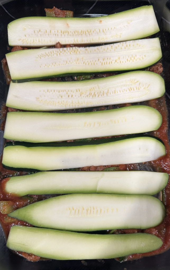 Image of sliced zucchini on top of tomato sauce.