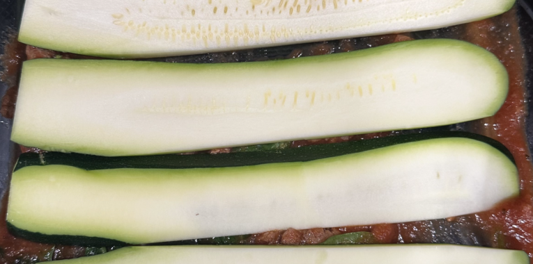 Image of sliced zucchini on top of tomato sauce.