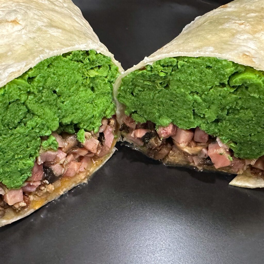 Image of a burrito on a black plate. The burrito contains a filling of eggs that are colored green, meat, and cheese.