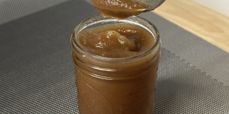 Image of jar filled with apple butter and a spoon with apple butter on it.