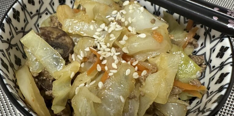 Image of small bowl with a cabbage and carrot mixture. Chopsticks are laying across the bowl.