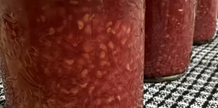 Image of 3 jars on a black and white gingham towel. The jars are filled with raspberry jam.